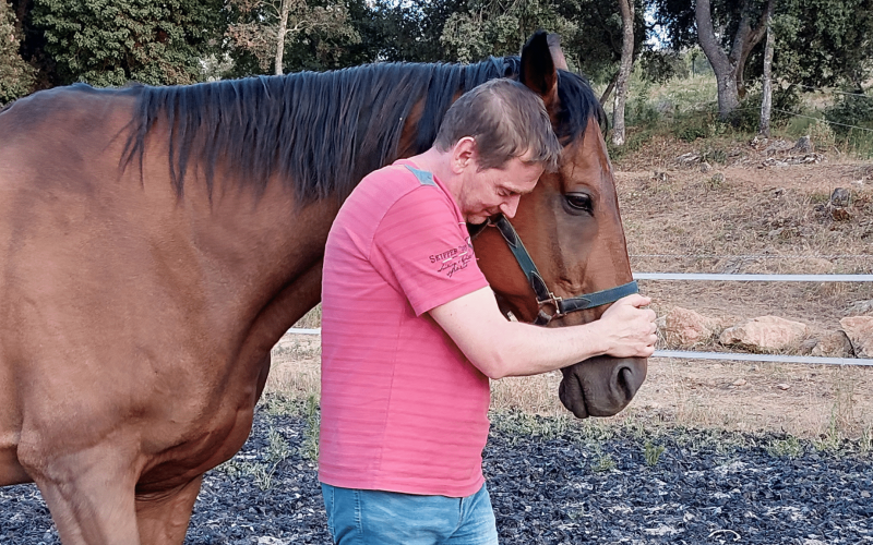 Homme exprimant une connexion émotionnelle avec un cheval dans un enclos, illustrant une approche thérapeutique dans une session d'équi-coaching holistique.