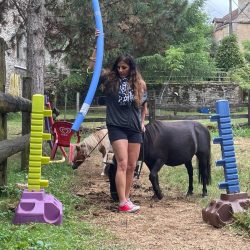 Femme guidant deux poneys à travers un parcours d'obstacles coloré en plein air, illustrant une session d'équi-coaching holistique dans un cadre rural.